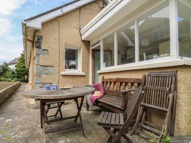 An outdoor seating area with a round wooden table with two mugs and a plate on it two wooden benches and folded wooden chairs at Yr Odyn in Llangrannog Ceredigion