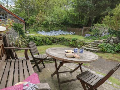 An outdoor seating area with wooden table and chairs on a patio surrounded by greenery at Yr Odyn in Llangrannog Ceredigion