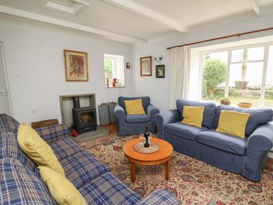 A living room with blue sofas yellow cushions a wood stove and a round wooden coffee table at Yr Odyn in Llangrannog Ceredigion