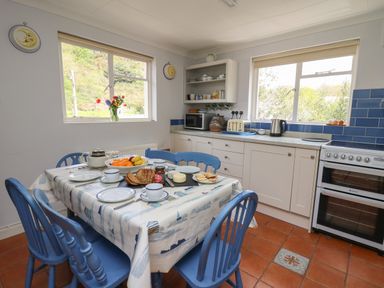 A kitchen with a dining table set with food and blue chairs at Yr Odyn in Llangrannog Ceredigion