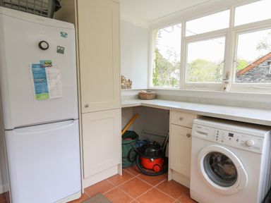 A utility room with a refrigerator, washing machine, countertop, cabinet, and vacuum cleaner under the counter at Yr Odyn in Llangrannog Ceredigion
