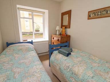 A bedroom with two single beds with map quilts a wooden chest of drawers a mirror and a window at Yr Odyn in Llangrannog Ceredigion