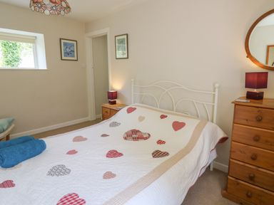 A bedroom with a bed with heart patterned quilt beside wooden chest of drawers and framed pictures on walls at Yr Odyn in Llangrannog Ceredigion