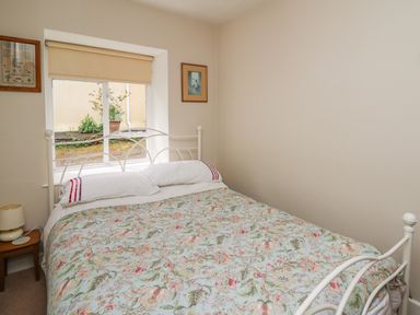 A bedroom with a bed with floral bedding a nightstand with a lamp and a window with a blind at Yr Odyn in Llangrannog Ceredigion