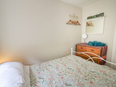 A bedroom with a bed covered by a floral quilt a wooden dresser with rolled towels and a small mirror and a wall-mounted rack with hangers at Yr Odyn in Llangrannog Ceredigion