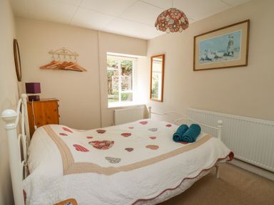 A bedroom with a white bed cover with hearts two rolled towels a wooden chest of drawers a window and a wall mirror at Yr Odyn in Llangrannog Ceredigion