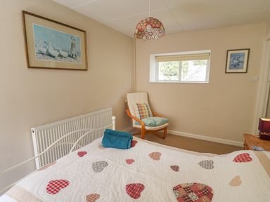 A bedroom with a bed with heart patterned quilt a wooden chair with cushions wall art and a window at Yr Odyn in Llangrannog Ceredigion