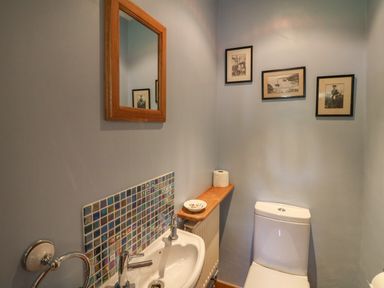 A small bathroom with a white toilet and sink a wooden shelf with a toilet paper and dish and a mirror above the sink at Yr Odyn in Llangrannog Ceredigion