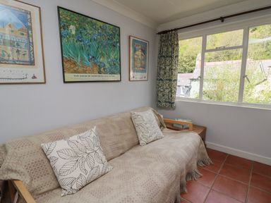 A sofa with patterned cushions and a throw next to a window with patterned curtains and framed artwork on the wall at Yr Odyn in Llangrannog Ceredigion