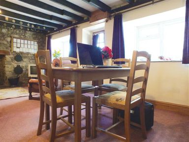 A dining room with a wooden table and chairs a laptop on the table stone wall and windows with dark curtains in Granston Cottage Castlemorris Pembrokeshire
