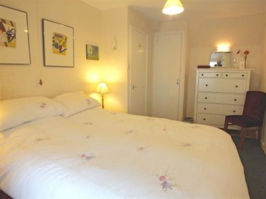 A bedroom with a double bed bedside lamp white chest of drawers purple chair and artworks on the wall at Granston Cottage in Castlemorris Pembrokeshire