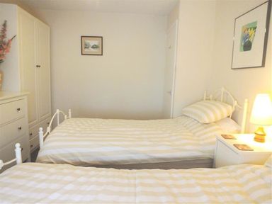 A bedroom with two single beds a white wardrobe a chest of drawers and framed pictures at Granston Cottage in Castlemorris Pembrokeshire