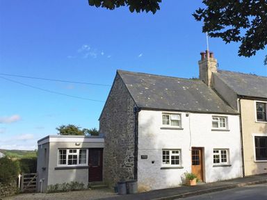 A two-story stone and white cottage with a small extension and a wooden door at Granston Cottage in Castlemorris Pembrokeshire