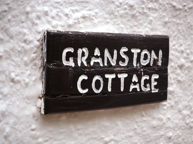A black wooden sign with white text reading Granston Cottage on a textured white wall at Granston Cottage in Castlemorris Pembrokeshire
