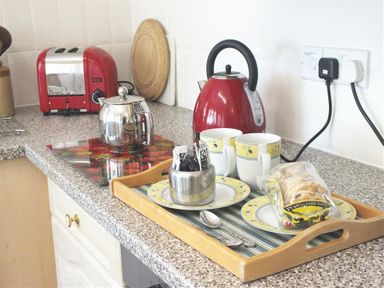 A kitchen countertop with a red kettle two mugs a teak tray with plates cutlery and sliced bread at Granston Cottage in Castlemorris Pembrokeshire