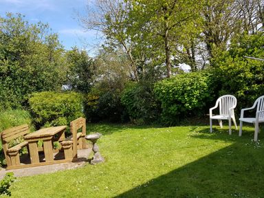A garden with a wooden table and benches and two white plastic chairs at Granston Cottage in Castlemorris Pembrokeshire