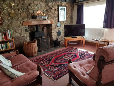 A sitting room with two armchairs a red patterned rug a fireplace stone wall a wooden TV stand with a television and a bookshelf at Granston Cottage in Castlemorris Pembrokeshire
