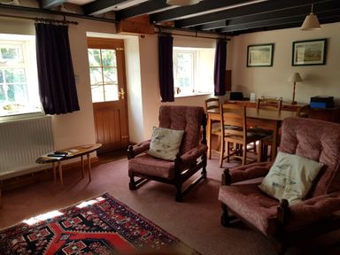 A living room with two armchairs a wooden dining table with chairs a side table with a lamp and two framed pictures on the wall at Granston Cottage in Castlemorris Pembrokeshire