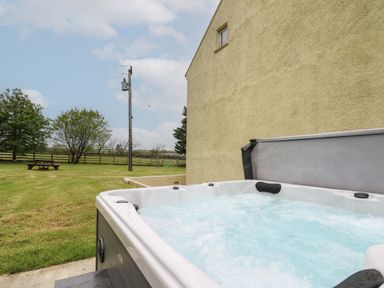 An outdoor hot tub with water bubbling next to a yellow building with a grassy yard and picnic table at Newton West Farm Newton near Newgale