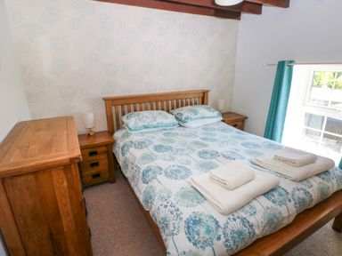 A bedroom with a wooden double bed with floral bedspread next to wooden bedside tables and a chest of drawers at Newton West Farm Newton near Newgale