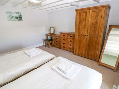 A bedroom with two single beds, wooden wardrobe, chest of drawers, dressing table with mirror, and standing mirror at Newton West Farm Newton near Newgale