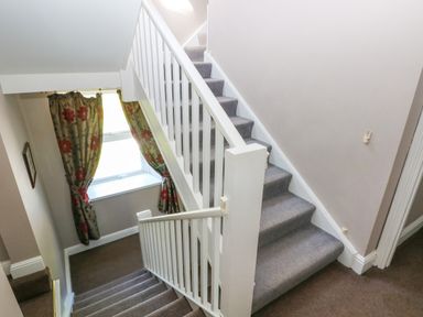 A carpeted staircase with white banisters and floral curtains on a window at Newton West Farm in Newton near Newgale