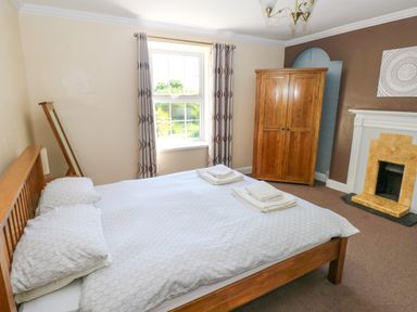 A bedroom with a wooden bed a window curtains a wooden wardrobe and a fireplace at Newton West Farm in Newton near Newgale