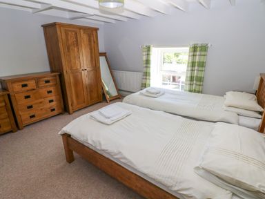 A bedroom with two single beds wooden furniture and a window with green plaid curtains at Newton West Farm in Newton near Newgale