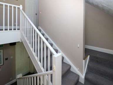 A staircase with white railings and grey carpet in a hallway at Newton West Farm in Newton near Newgale