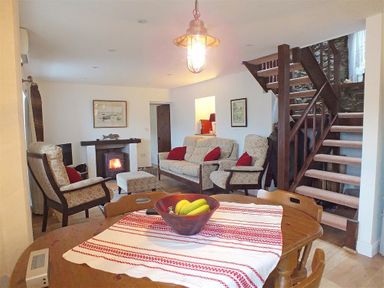 A living room with armchairs a sofa a wood burning stove and a wooden staircase at Beach Cottage in Little Haven Pembrokeshire