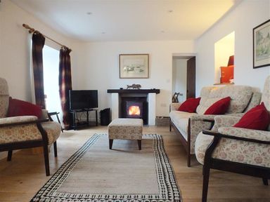 A living room with floral patterned sofas red cushions a rug a fireplace and a television at Beach Cottage in Little Haven Pembrokeshire