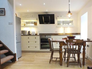 A kitchen with wooden chairs and table and appliances including oven refrigerator and kettle at Beach Cottage in Little Haven Pembrokeshire