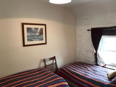 A bedroom with two striped beds a wooden chair a framed picture on the wall and a window with curtains at Beach Cottage in Little Haven Pembrokeshire