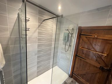 A shower with glass panels and a wooden door at Beach Cottage in Little Haven, Pembrokeshire