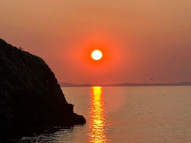 A sunset over water with a cliff on the left at Beach Cottage in Little Haven, Pembrokeshire