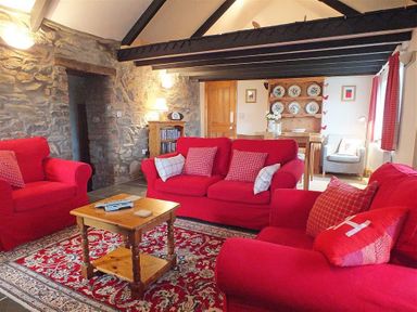 A living room with red sofas a wooden coffee table a stone wall and a wooden dresser with plates at Gwndwn Gwyn in Trefasser Near Strumble Head