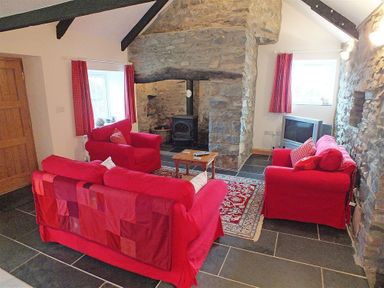 A living room with red sofas a stone fireplace wooden coffee table and a television at Gwndwn Gwyn in Trefasser Near Strumble Head