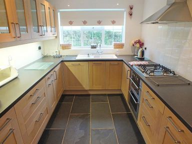 A kitchen with wooden cabinets gray countertops a window above the sink and a stovetop at Gwndwn Gwyn in Trefasser Near Strumble Head