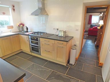 A kitchen with wooden cabinets a gas stove oven and toaster adjacent to a living room with a red sofa at Gwndwn Gwyn in Trefasser Near Strumble Head