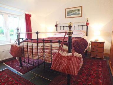 A bedroom with a metal bed frame two red patterned bags on bedposts wooden bedside table with lamp and framed picture on wall at Gwndwn Gwyn in Trefasser Near Strumble Head