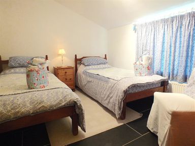 A bedroom with two single beds a wooden nightstand lamp a chair and curtains at Gwndwn Gwyn in Trefasser Near Strumble Head
