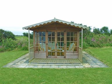 A wooden garden summerhouse with glass doors and wicker furniture on a stone patio surrounded by grass at Gwndwn Gwyn Trefasser Near Strumble Head