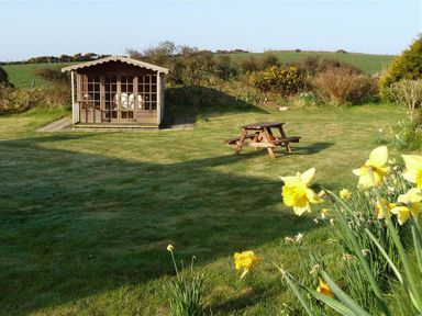 A garden with a wooden summerhouse a picnic table and yellow flowers in the foreground at Gwndwn Gwyn in Trefasser Near Strumble Head