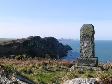 A stone memorial standing on grassy land overlooking cliffs and the sea at Gwndwn Gwyn Trefasser Near Strumble Head