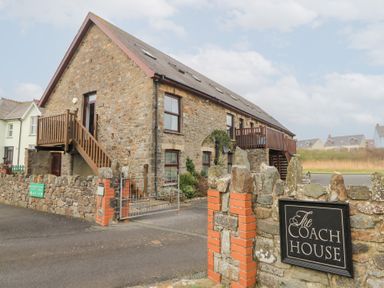 A stone building with external wooden staircases and a sign reading The Coach House at 5 The Coach House in Broad haven Pembrokeshire