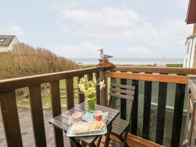 A balcony with a wooden table and chair a tray with cups and biscuits and flowers in a vase overlooking the sea at 5 The Coach House in Broad haven Pembrokeshire