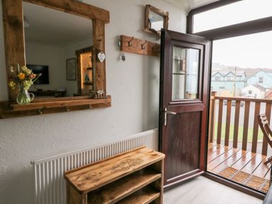 An entryway with a wooden shoe rack and mirror next to an open door leading to a balcony at 5 The Coach House Broad haven Pembrokeshire