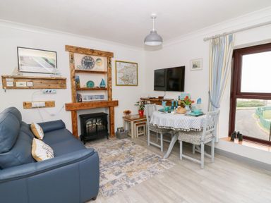 A living room with a blue sofa a dining table set for four a wall mounted TV and a window with striped curtains at 5 The Coach House Broad haven Pembrokeshire
