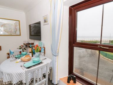 A dining area with a table set for two near a window overlooking a beach at 5 The Coach House Broad haven Pembrokeshire
