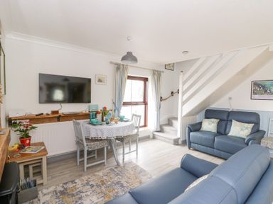 A living room with blue sofas dining table under window and stairs at 5 The Coach House in Broad haven Pembrokeshire